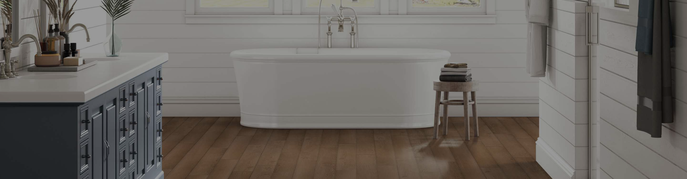Modern bathroom with a white soaking tub, chrome fixtures, warm wood flooring, shiplap walls, large windows, and natural light creating a serene, luxurious atmosphere.